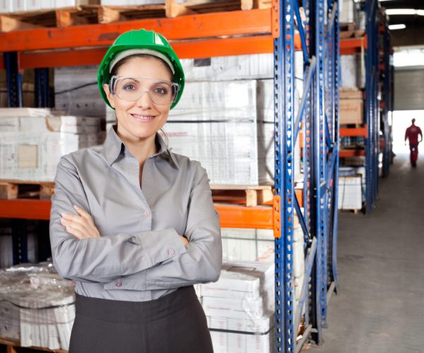 Portrait of young female supervisor wearing protective eyeglasses with arms crossed at warehouse